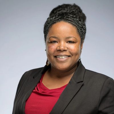 Smiling photo of Melinda wearing a red dress and black blazer