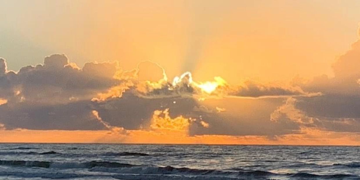 Sunset over the ocean with clouds illuminated by golden light.