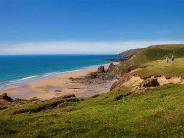 Scenic coastal view with grassy cliffs and sandy beach under clear blue sky.