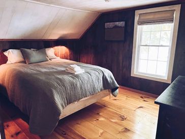 Cozy attic bedroom with wooden walls, a large bed, and natural light from a window.