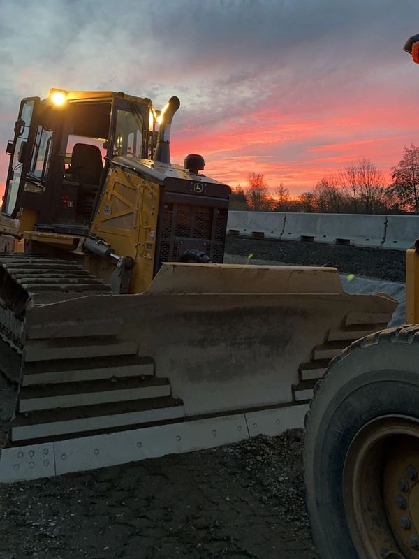 Yellow bulldozer at a construction site during sunset with lights on.