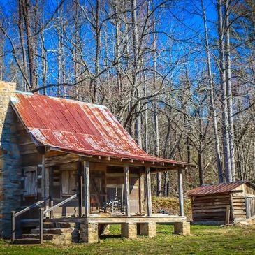 Rustic wooden cabin with a red metal roof in a leafless forest.
