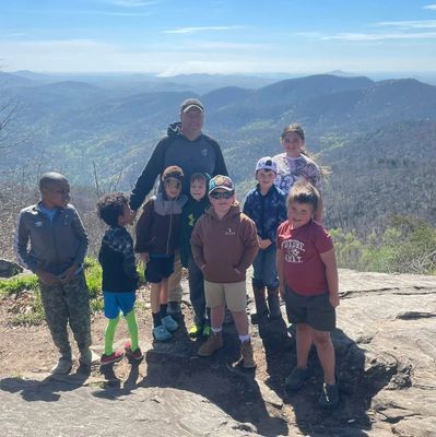 Group of kids and two adults posing on a mountain overlook with scenic views.