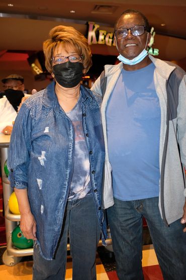 Two people posing indoors, one wearing a mask.