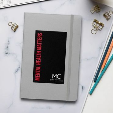 Gray and black Journal book on desk with white keyboard cup of coffee and pencils