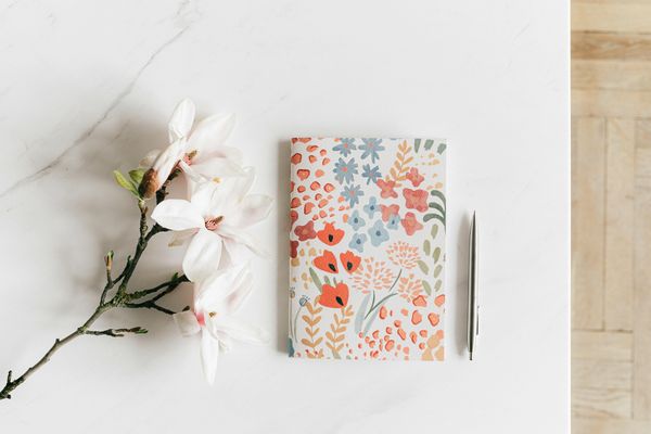 3 magnolia Blooms on single stem next to a  floral Journal a silver pen on a white quarts counter