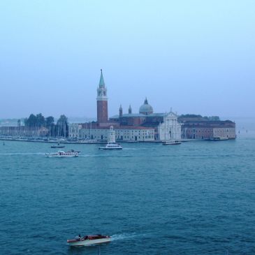 Island with historic buildings and boats in water.