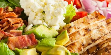 A close-up of a grilled chicken salad with avocado, bacon, and cauliflower.