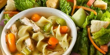 A bowl of chicken noodle soup with a fresh side salad.