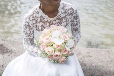 Bride in lace dress holding bouquet of pink and white roses.