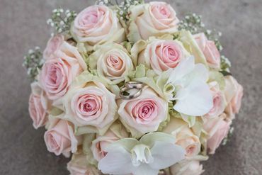 Bouquet of pale pink roses with white orchids and wedding rings.
