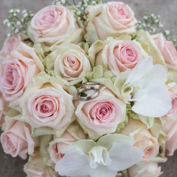Wedding rings on a bouquet of pale pink roses.