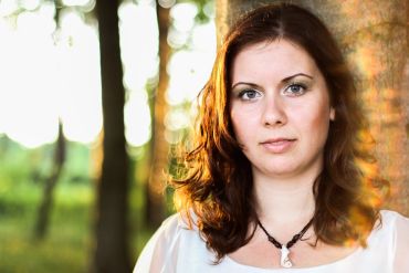 Woman with brown hair leaning against a tree.