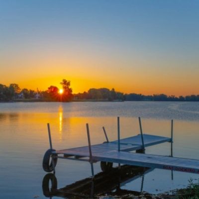 Sunset over calm lake near a dock.