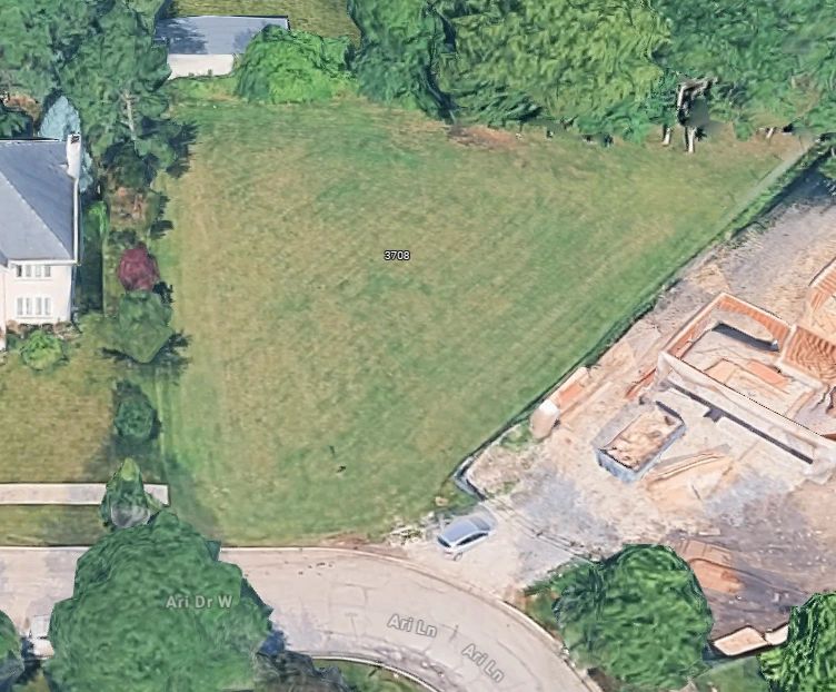 Aerial view of a green lot between houses and a construction site.