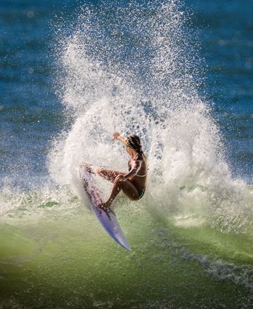 Surfer performing a dynamic turn on a wave with water spray surrounding.