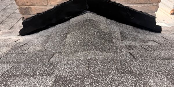 Newly installed gray asphalt shingles roof corner with black waterproofing.