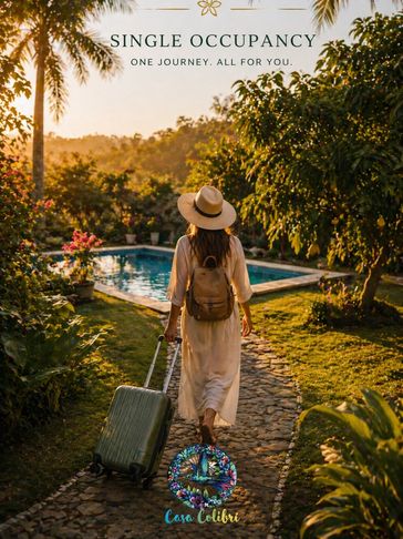 Woman walking with suitcase towards a pool in a lush garden at sunset.