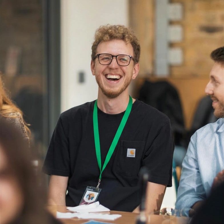 A young man with glasses laughing joyfully in a casual meeting.
