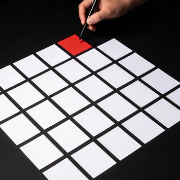 Hand holding pen over red sticky note among white ones on black surface.