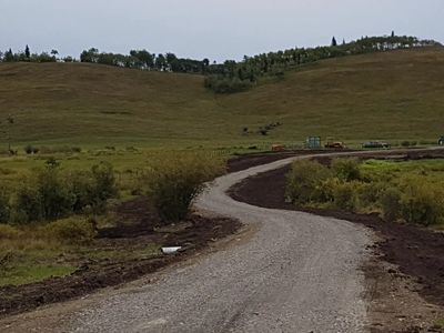 A winding gravel road through grassy hills under a cloudy sky.