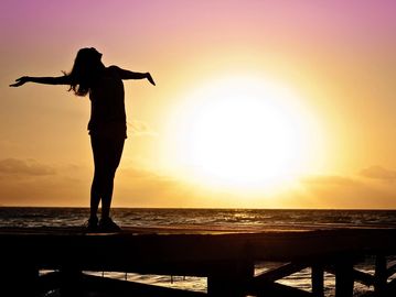 Person enjoying a sunset with arms outstretched on a pier.