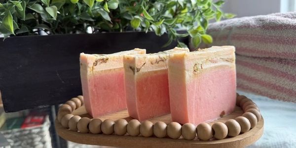 Three handcrafted pink and cream soap bars on a wooden bead tray.