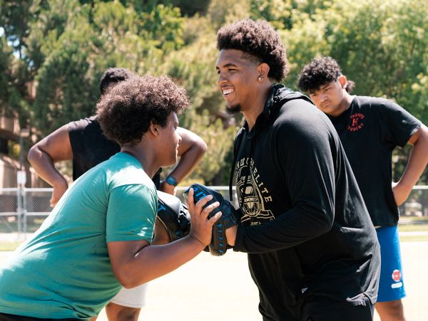 Two young men smiling and practicing football with focus from teammates in the background.