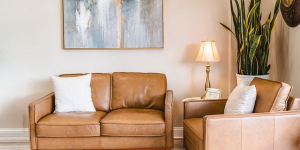 Cozy living room with tan leather sofa and armchair, accented by white pillows and a tall plant.