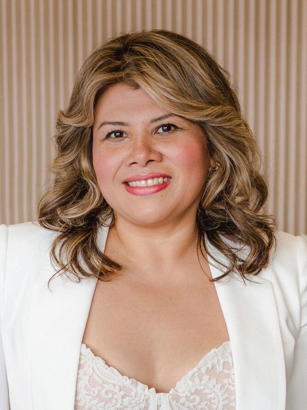 Smiling woman with styled hair in white blazer and lace top.
