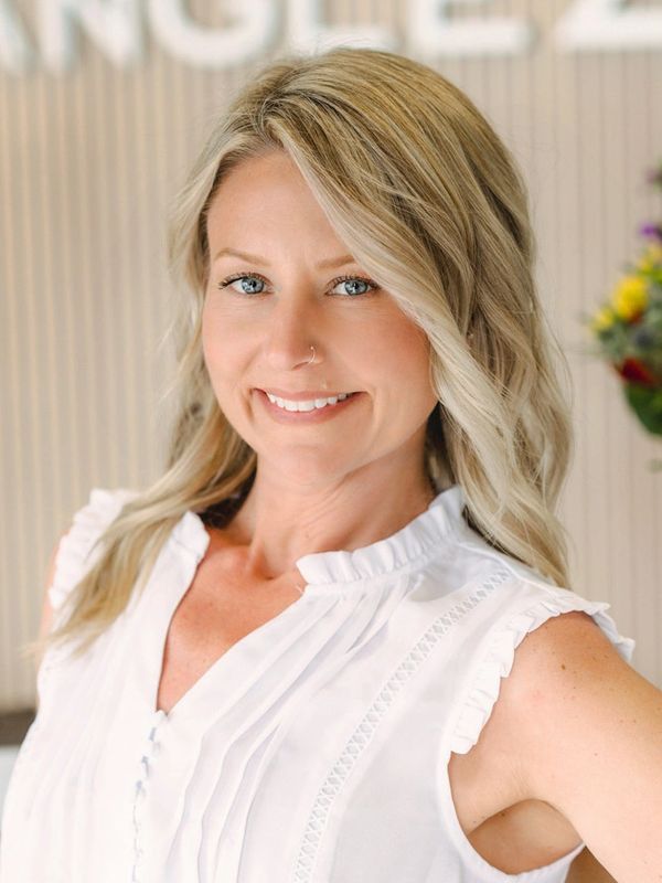 Smiling woman with blonde hair and blue eyes in white blouse.