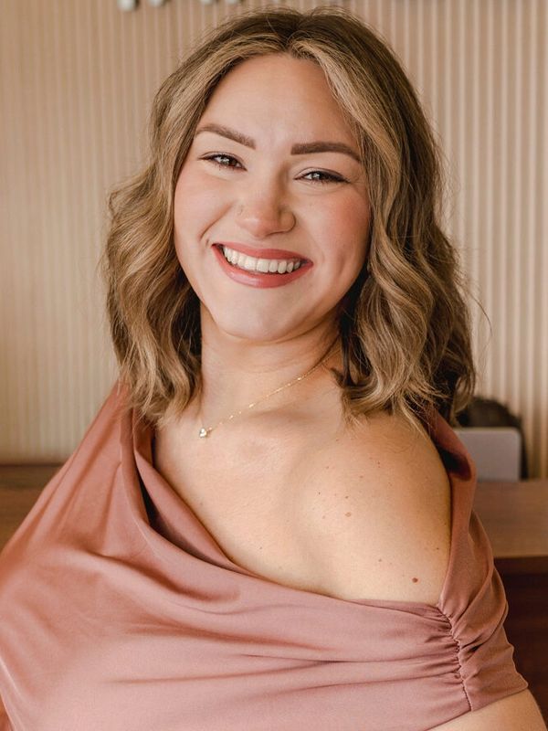 Smiling woman with wavy hair wearing an off-shoulder top.