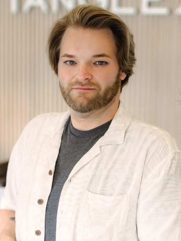 Man with beard wearing a white shirt and gray t-shirt posing indoors.