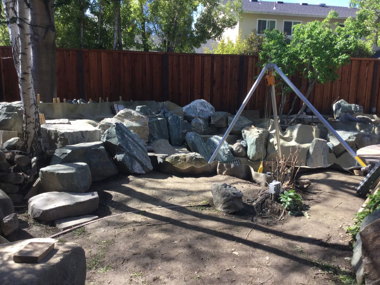 Backyard with large rocks, dirt, and a tripod structure.