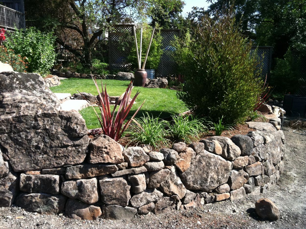 Stone wall with garden and grass inside.