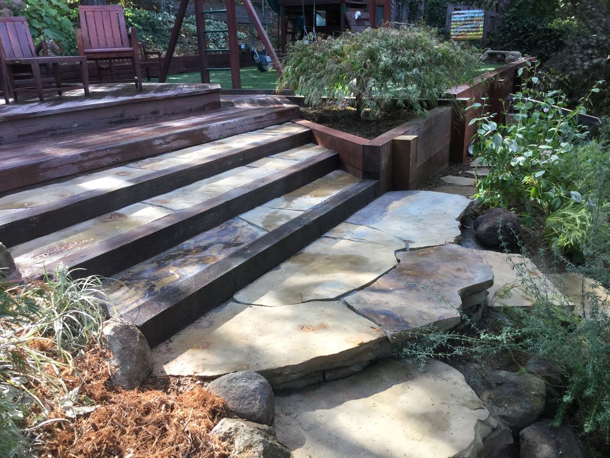 Wooden stairs leading to a garden with stone pathway and greenery.