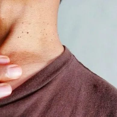 Close-up of a person touching their neck wearing a brown shirt.