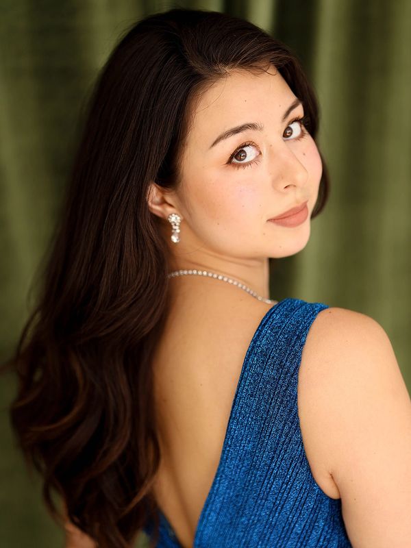 A woman in an elegant blue dress looks over her shoulder with a soft expression.