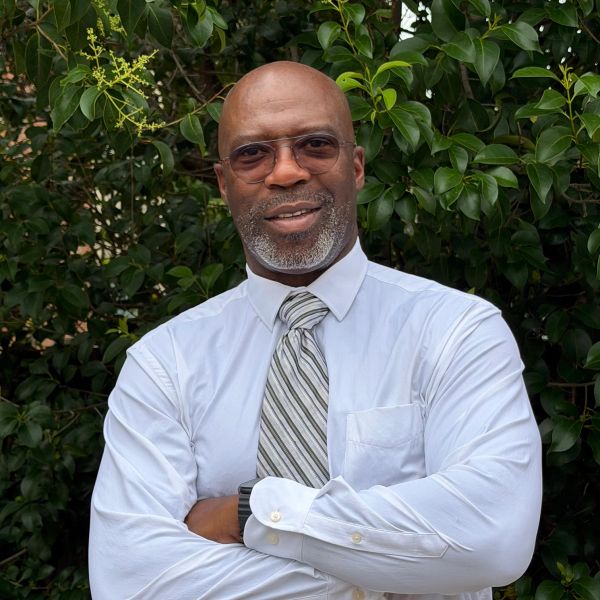 Man in white shirt and tie standing with arms crossed.