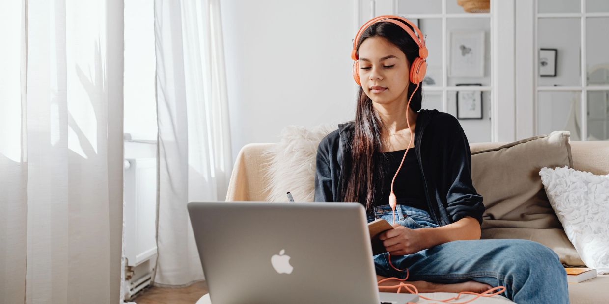 Woman with headphones working on a laptop and writing notes.