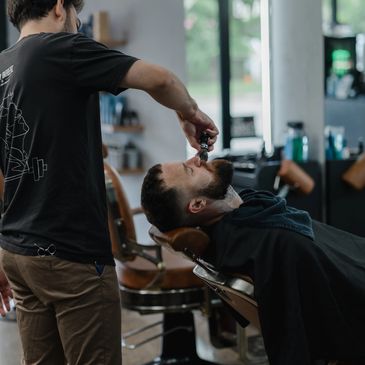 Barber applying shaving cream to a client's beard in a modern barbershop.