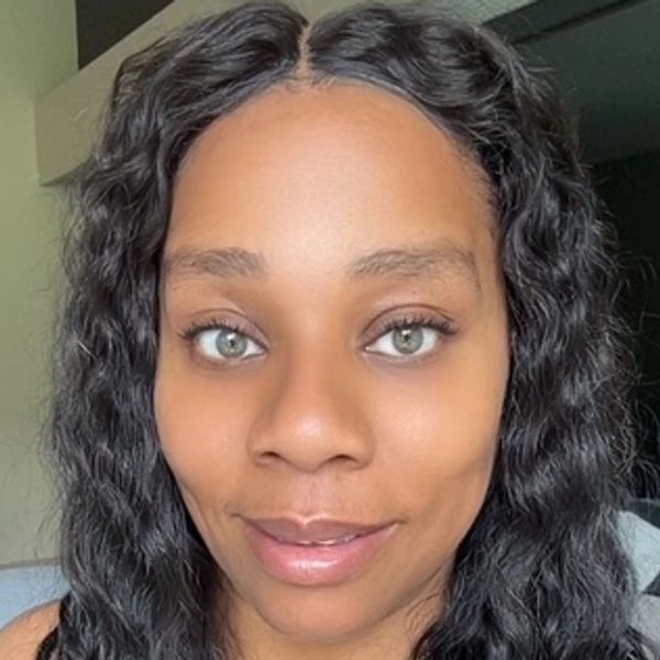 Close-up portrait of a woman with curly black hair and green eyes.