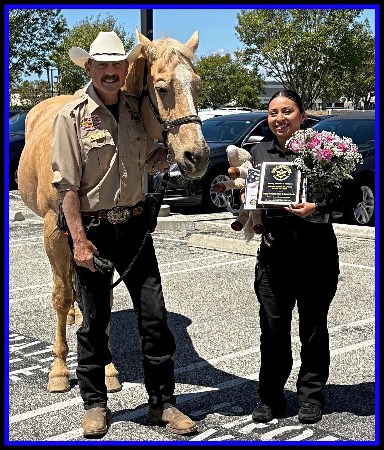 A sheriff with a horse stands next to a smiling officer holding flowers and a plaque.