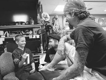 Man with tattoos smiling at a boy in a tattoo parlor.