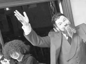 Two people posing happily indoors, one with a big beard and suit.