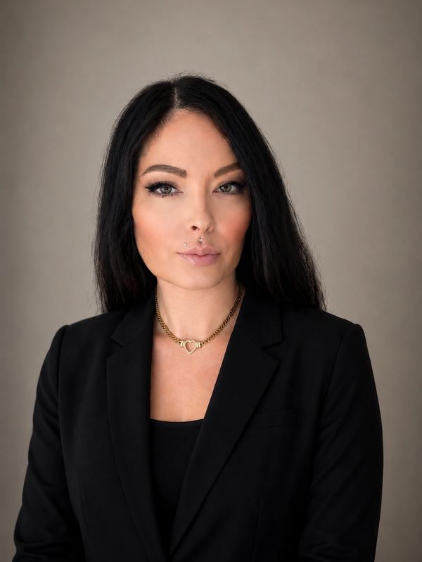 Confident woman with dark hair in a black blazer and gold necklace.