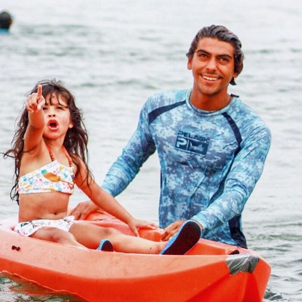 Man standing in water, smiling and holding a canoe with a little girl pointing at something. 