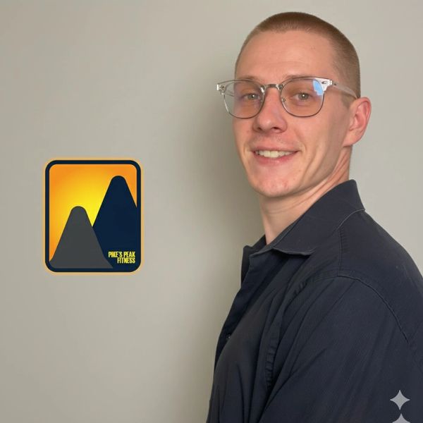 Smiling man with glasses posing beside a Peak's Peak Fitness logo on a plain wall.