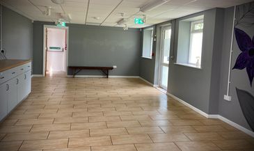 Empty room with tiled floor and gray walls, featuring a bench and exit signs.