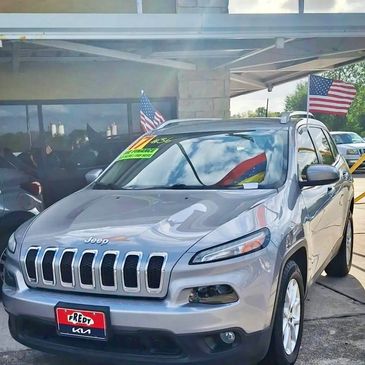 Silver Jeep SUV with American flags and dealership tag.